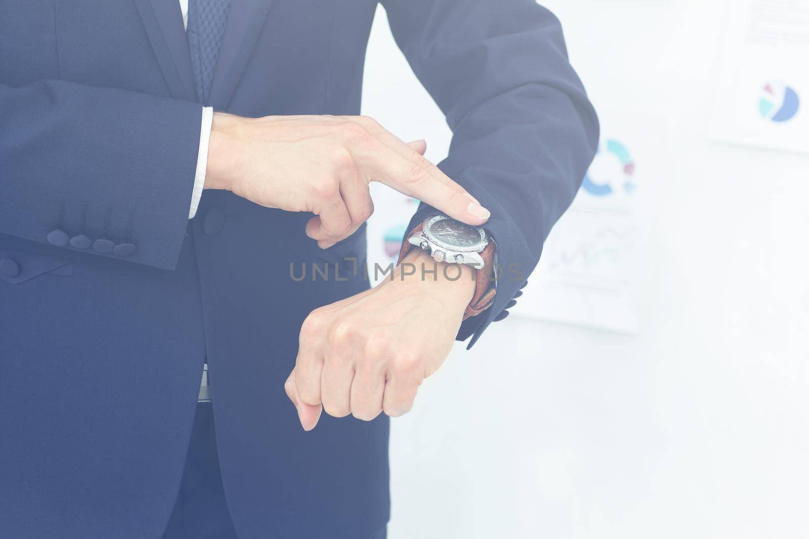 on the left side of the photo close-up of businessman with finger point at his watch in his hand. on the right side of the photo on the background of the financial schedules there is empty space for your text