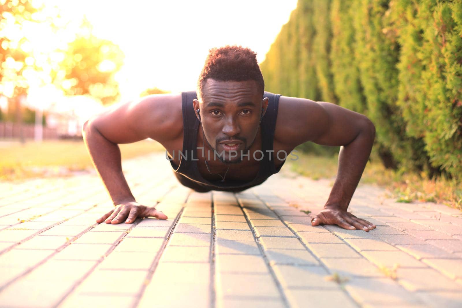 African man in sports clothing keeping plank position in beach while exercising outdoors, at sunset or sunrise. by tsyhun