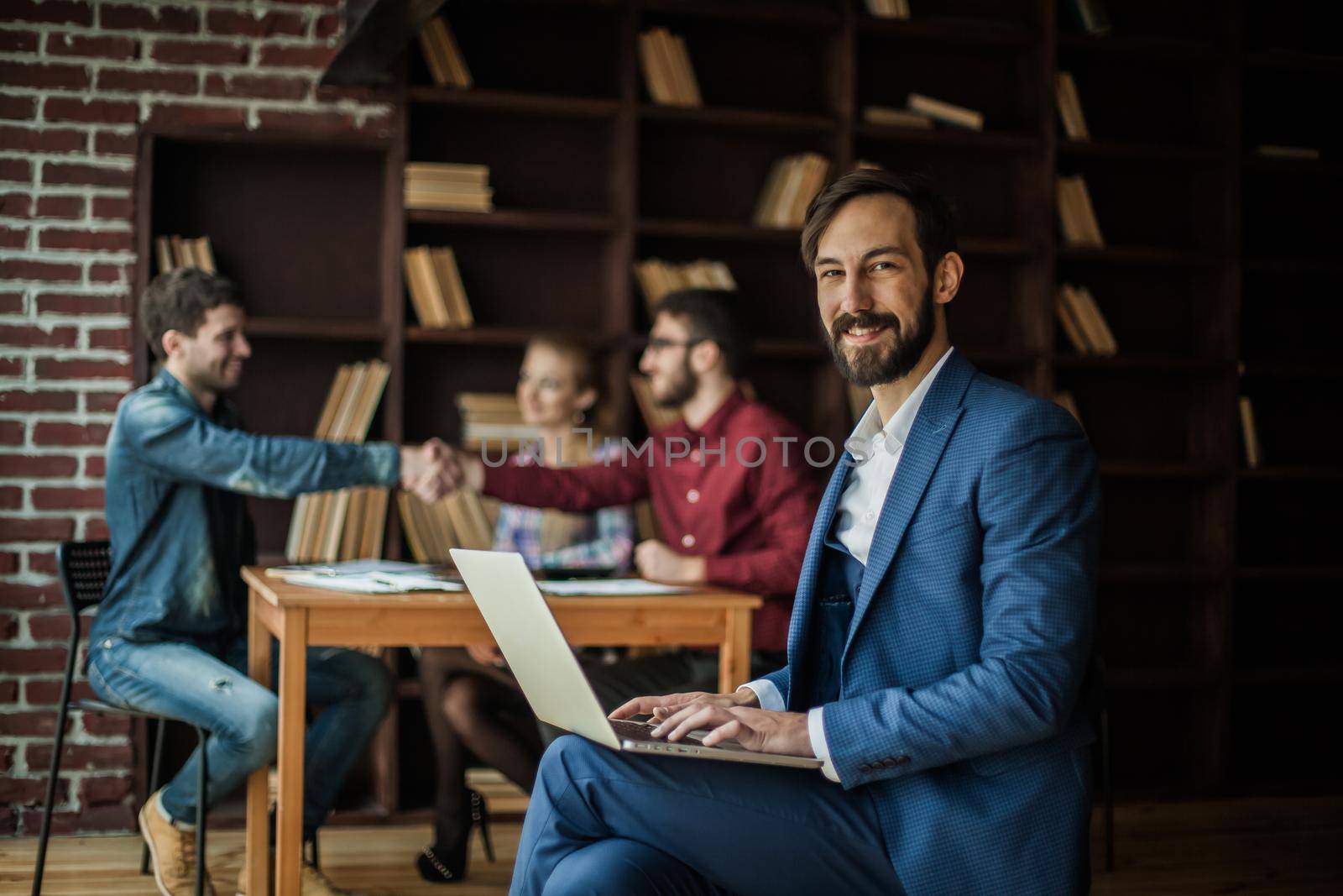 Manager Finance works with the marketing graphics on the laptop on the background of business partners handshaking in the workplace in the office