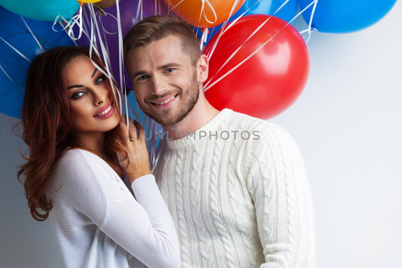 Young smiling couple with colorful balloons on white