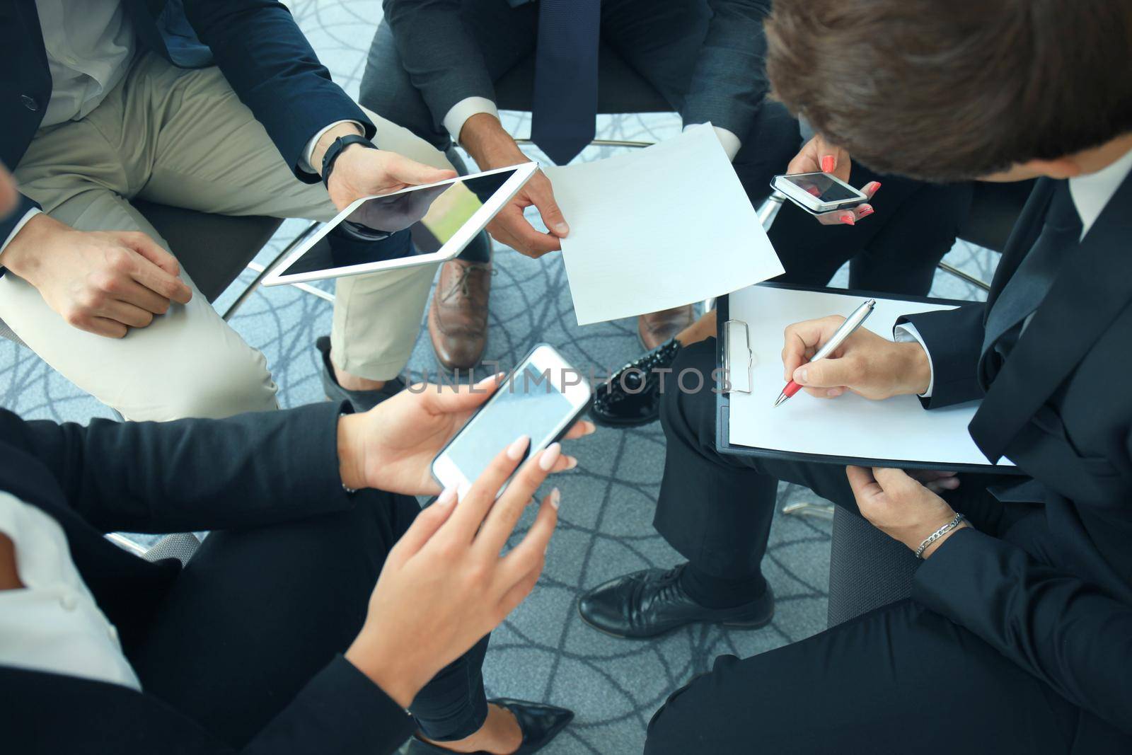 Group of people using smart phones sitting at the meeting, close up on hands.