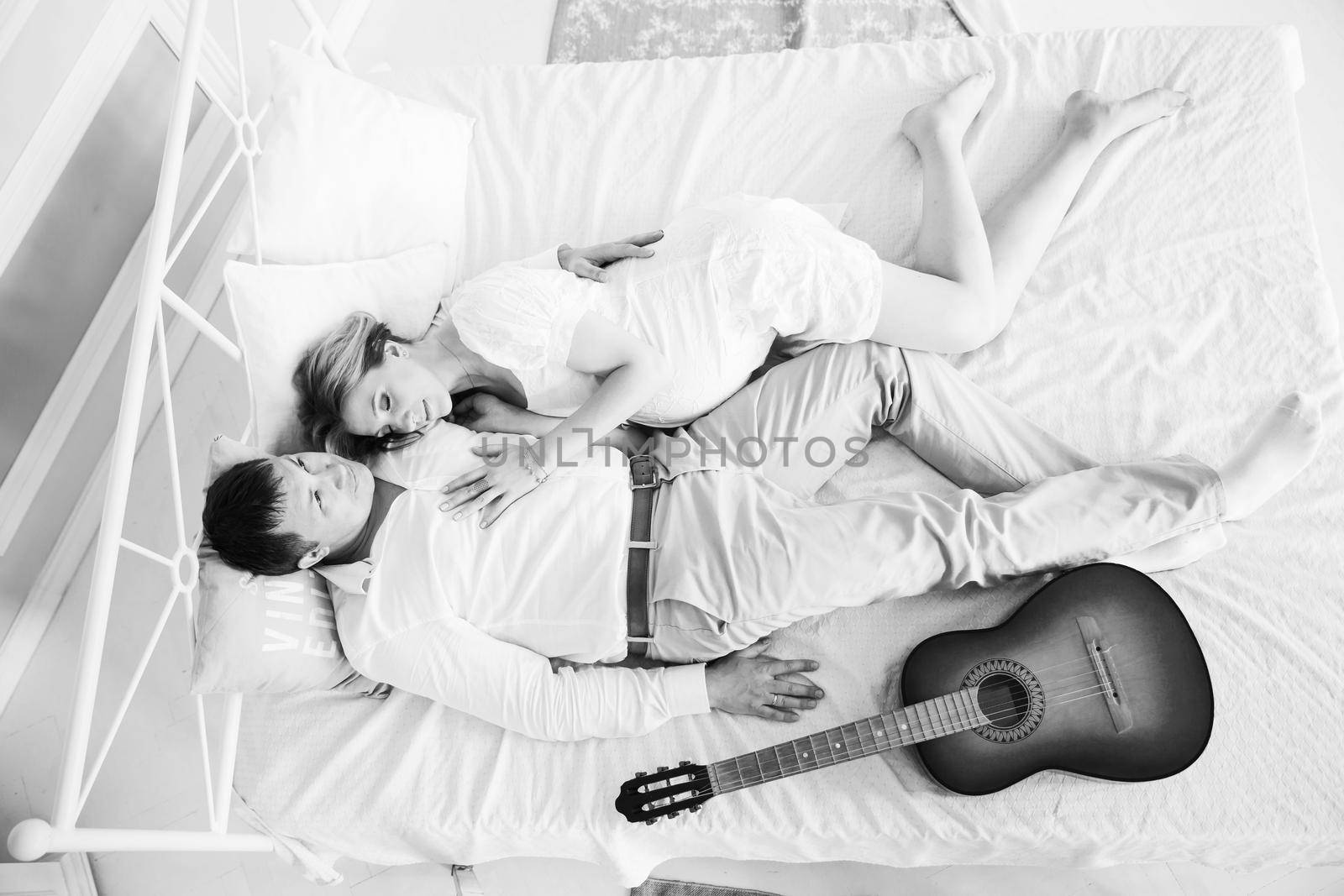 loving husband with a guitar and his pregnant wife in bed in a beautiful interior. Black and white photo