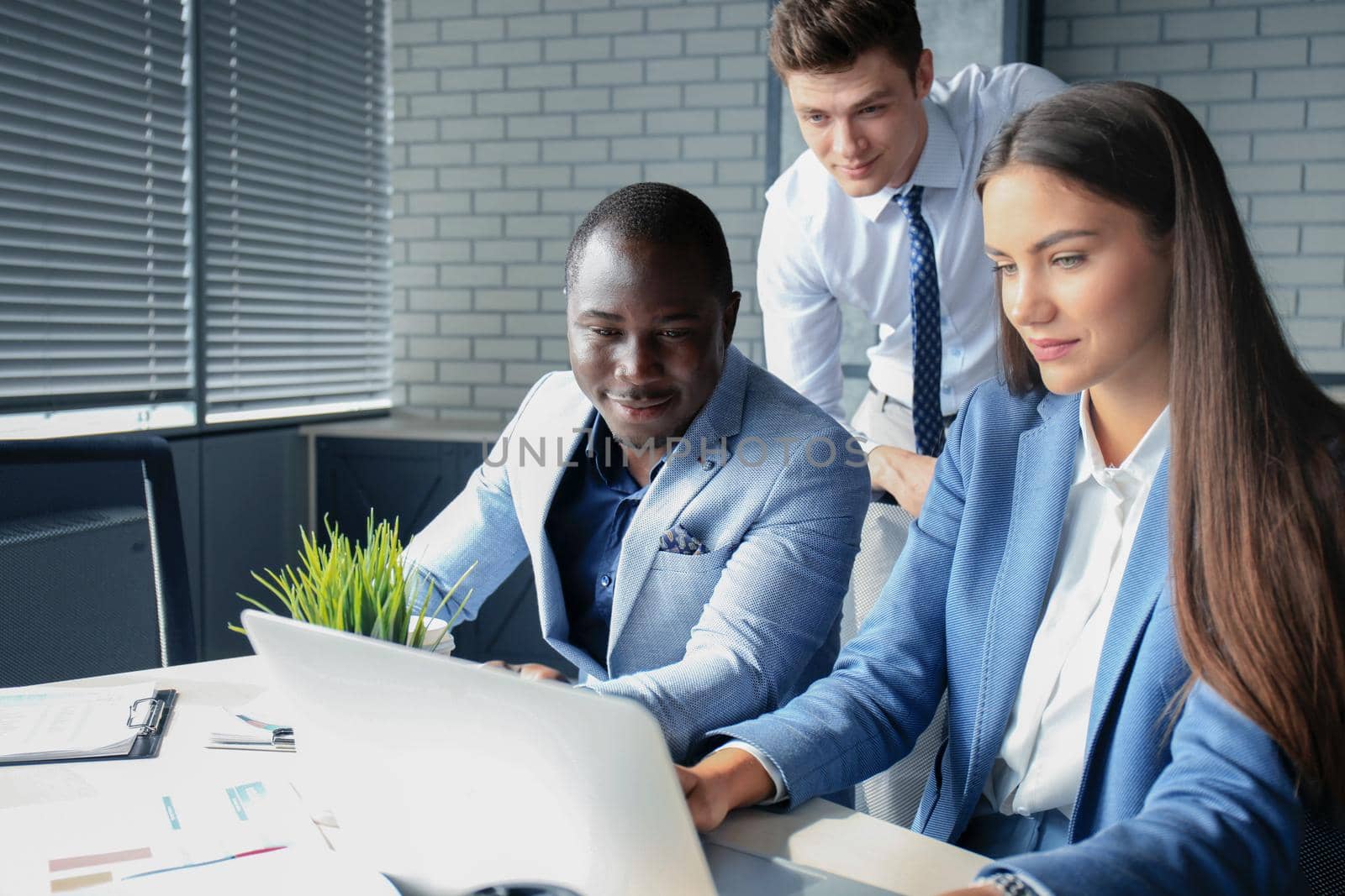 Business woman standing in foreground with a tablet in her hands, her co-workers discussing business matters in the background