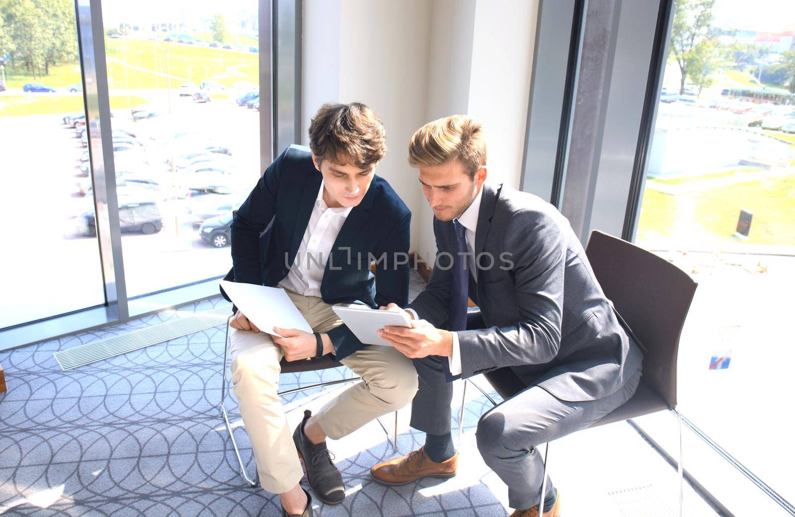 Mature businessman using a digital tablet to discuss information with a younger colleague in a modern business office.