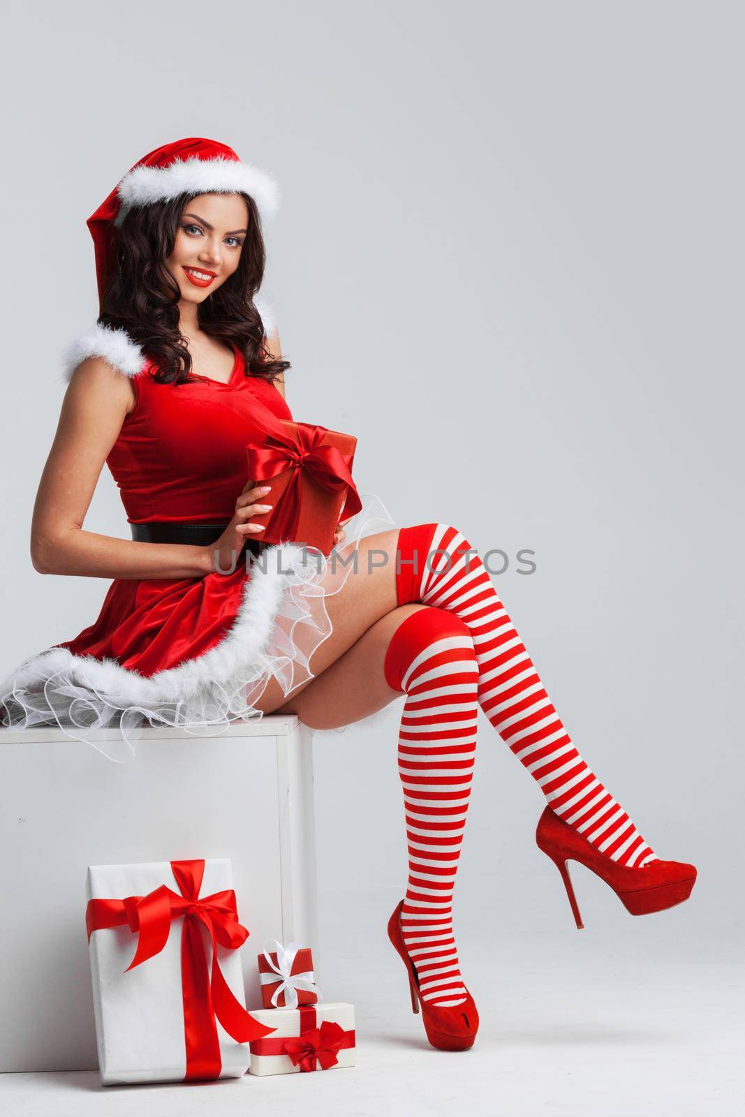 Beautiful young pin-up girl in santa dress sitting near christmas presents