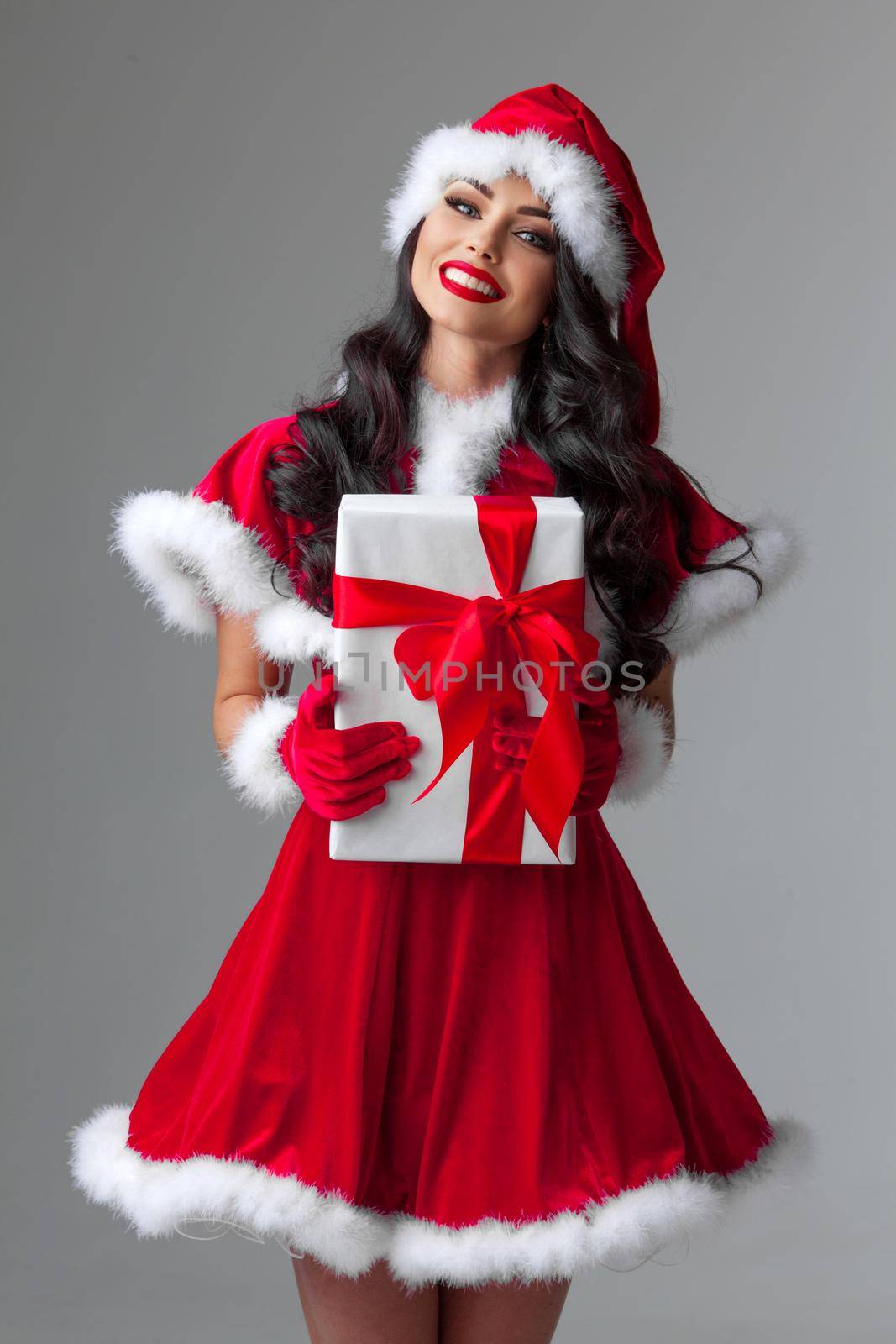 Beautiful young woman in Santa dress celebrating Christmas holding gift box