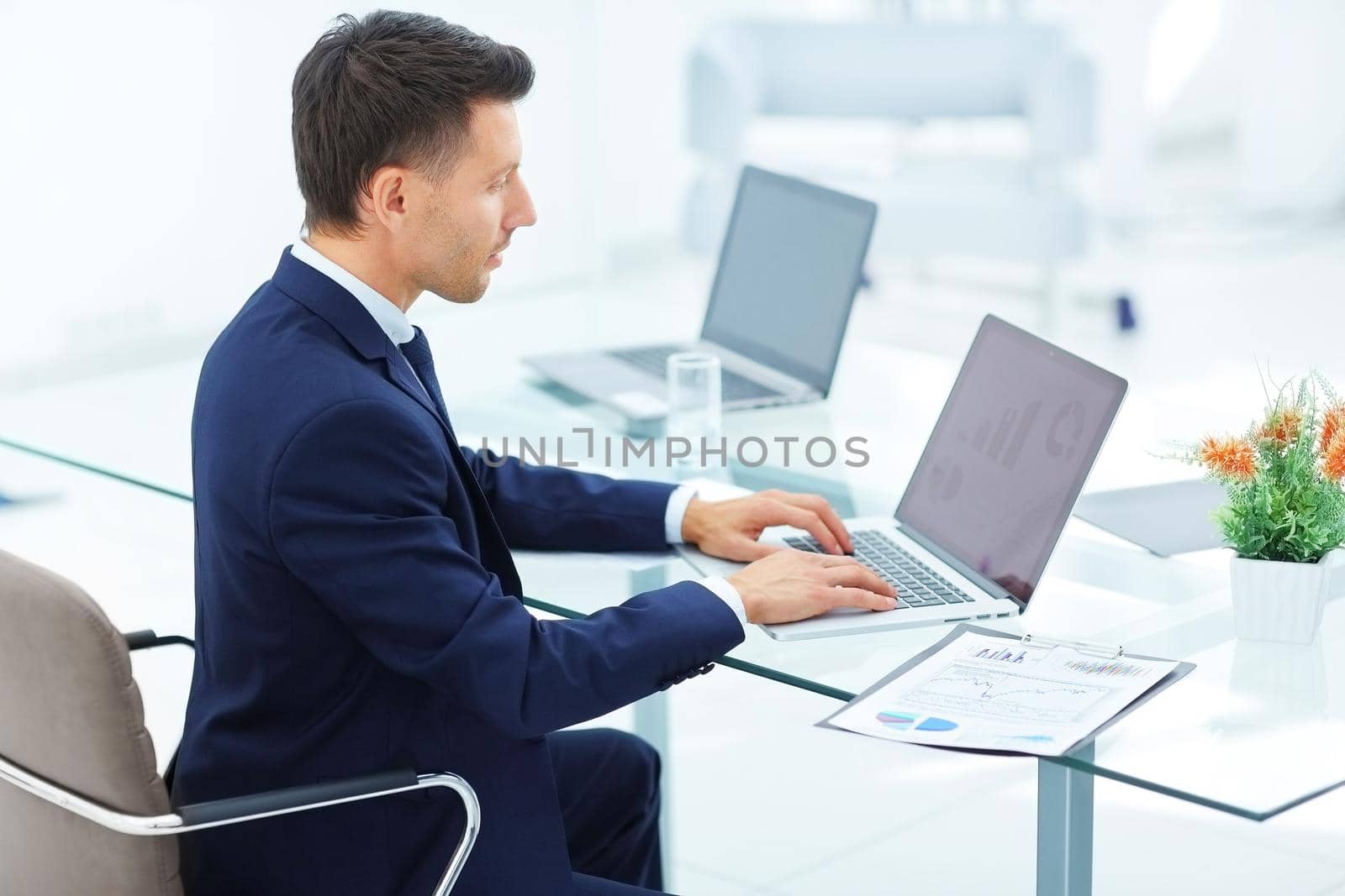 accountant was sitting at the table in front of the open laptop. On the screen of the laptop - financial charts. on the table laid out financial documents