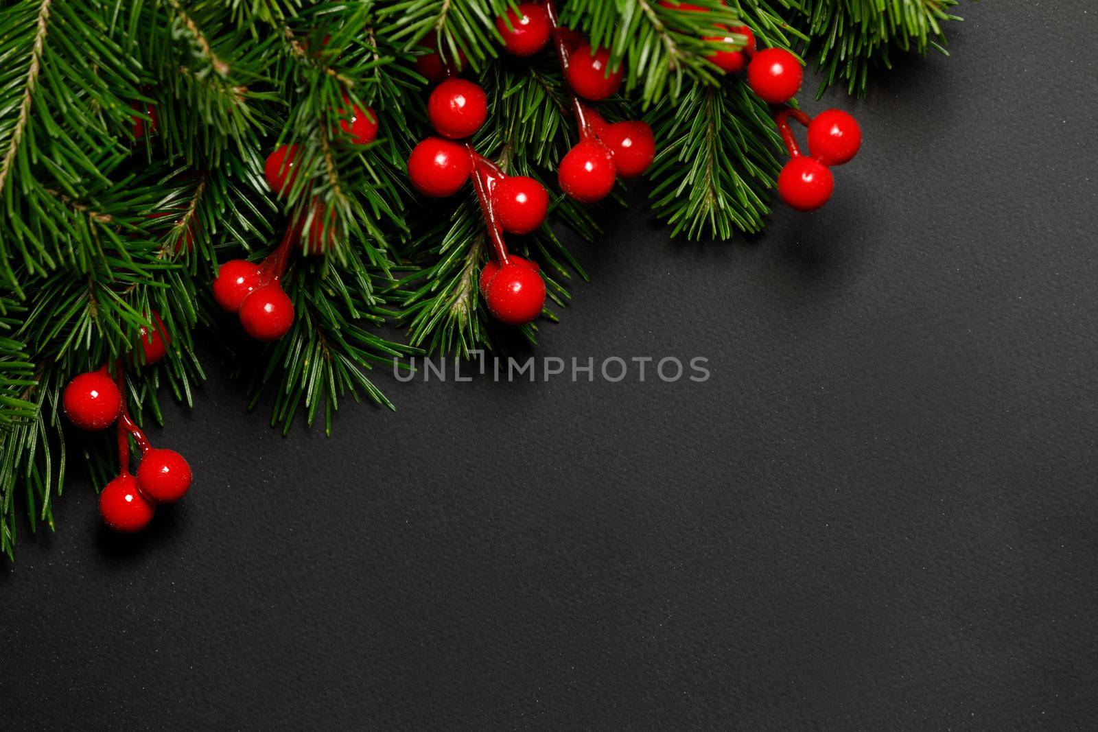 Christmas border arranged with fresh fir branches and red berries on black paper background , copy space for text