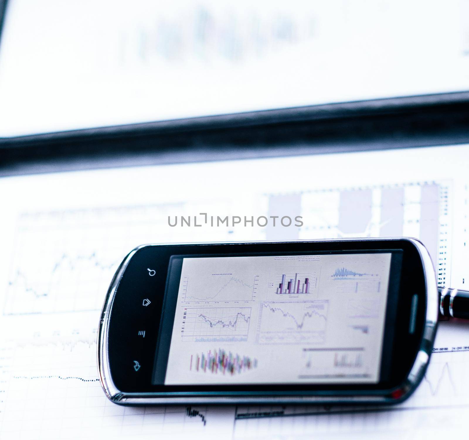 Business chart with a smart phone and a pen on a desk in the off by SmartPhotoLab