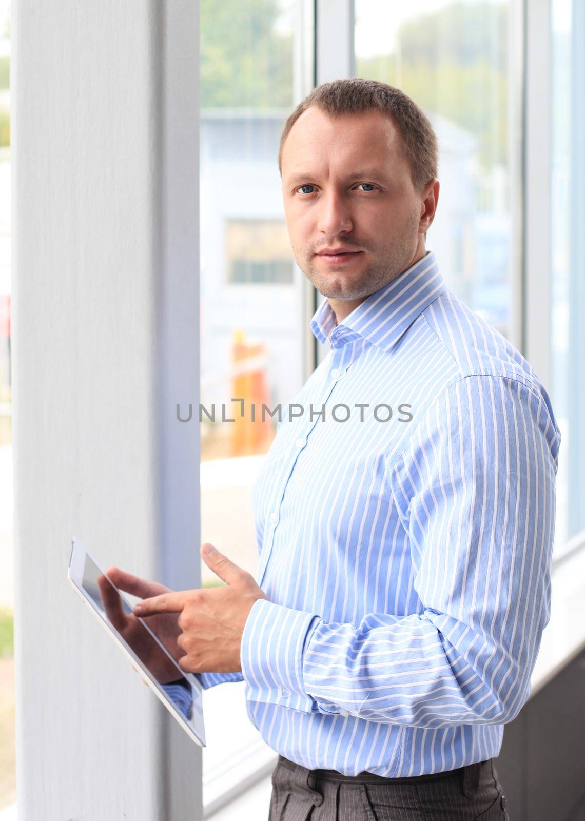 Closeup of a young business man at his office and using his modern tablet pc to do his work by tsyhun