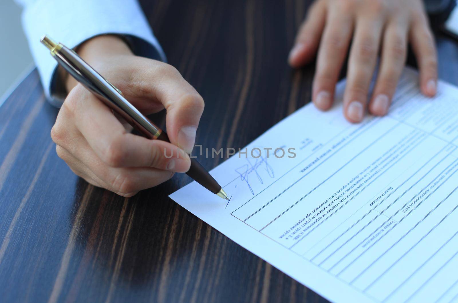 Businesswoman sitting at office desk signing a contract with shallow focus on signature.