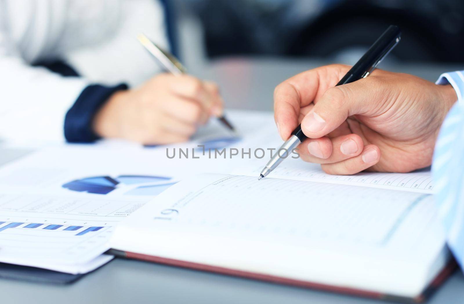 Unrecognizable business person analyzing graphs and taking notes by tsyhun
