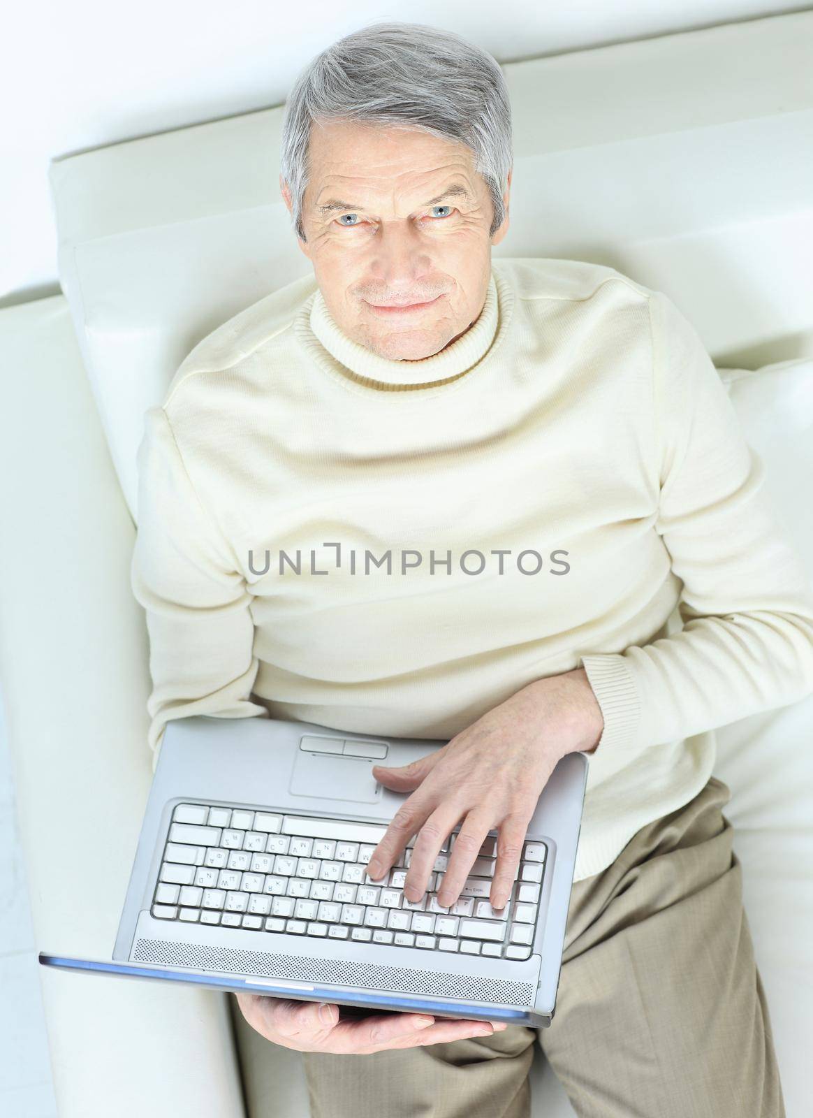 Happy elderly man at home with laptop on sofa looking up