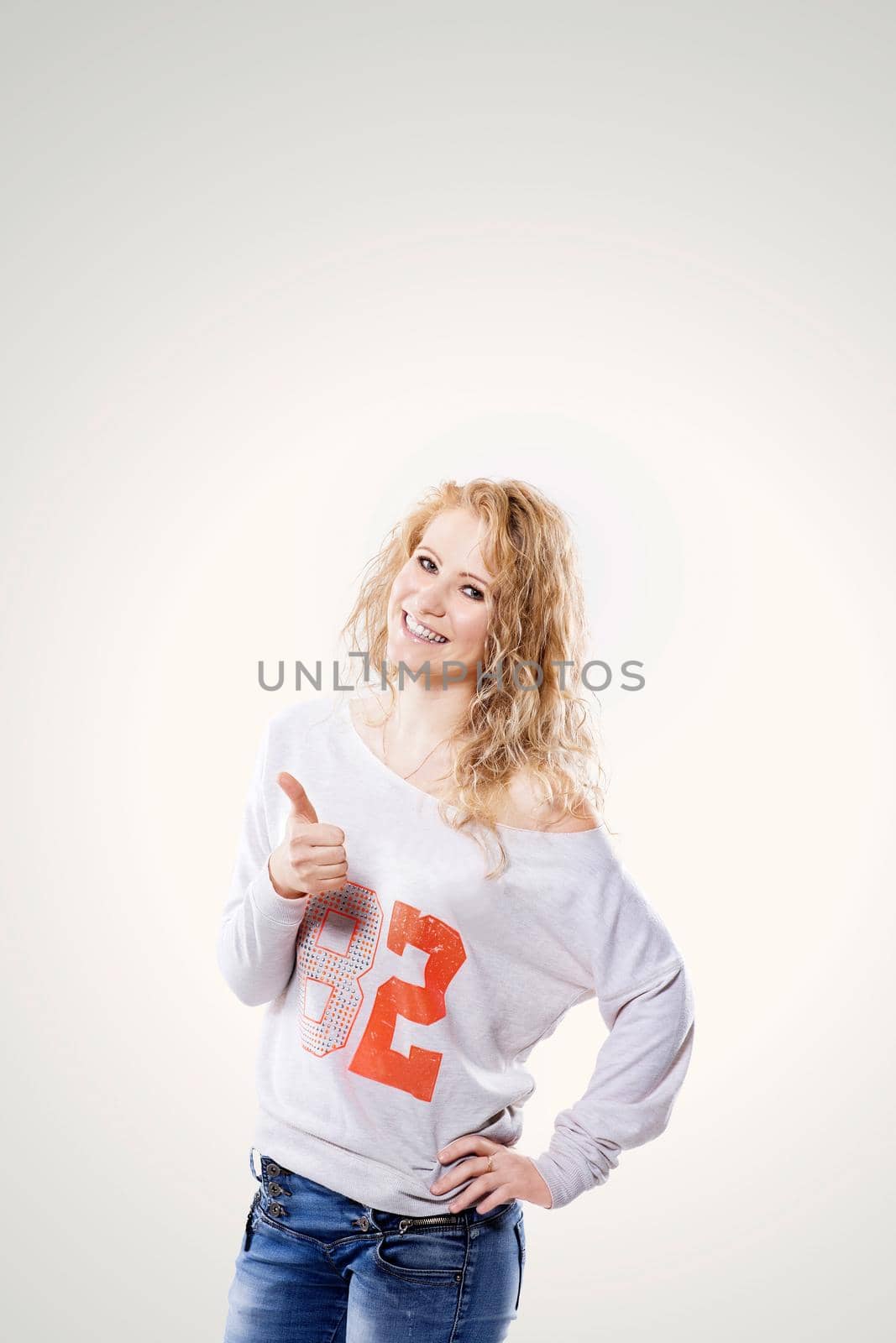 Beautiful young blond woman in jeans and t-shirt showing a thumbs up on a white background