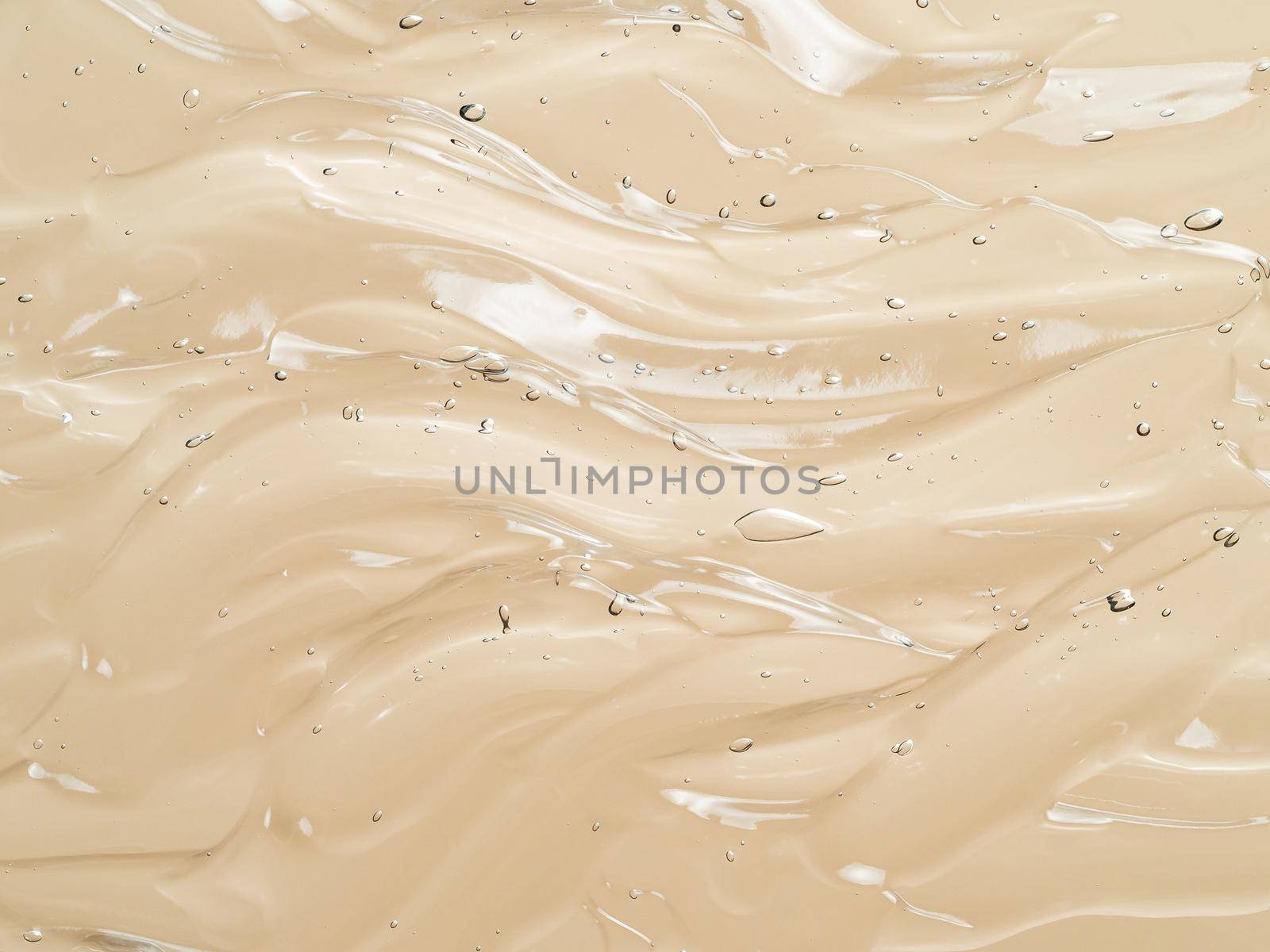 Liquid gel cosmetic texture on beige nude background. Aesthetic beautiful textured smears transparent skin gel with waves. Top view or flat lay. Champagne color gel background
