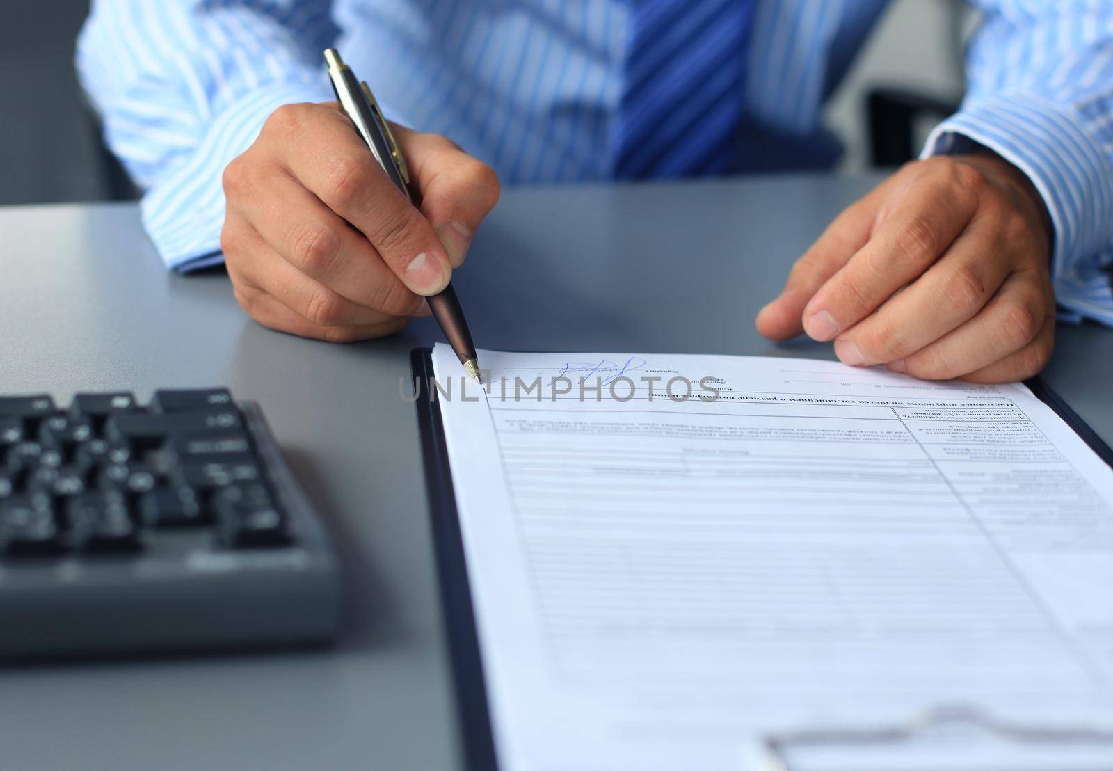 Businessman sitting at office desk signing a contract with shallow focus on signature. by tsyhun