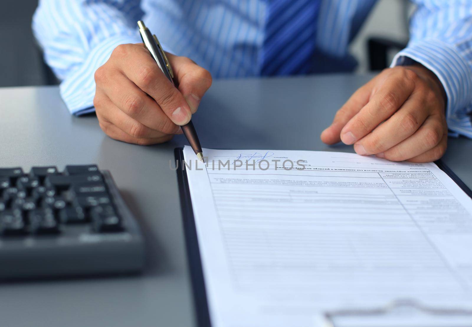 Businessman sitting at office desk signing a contract with shallow focus on signature.