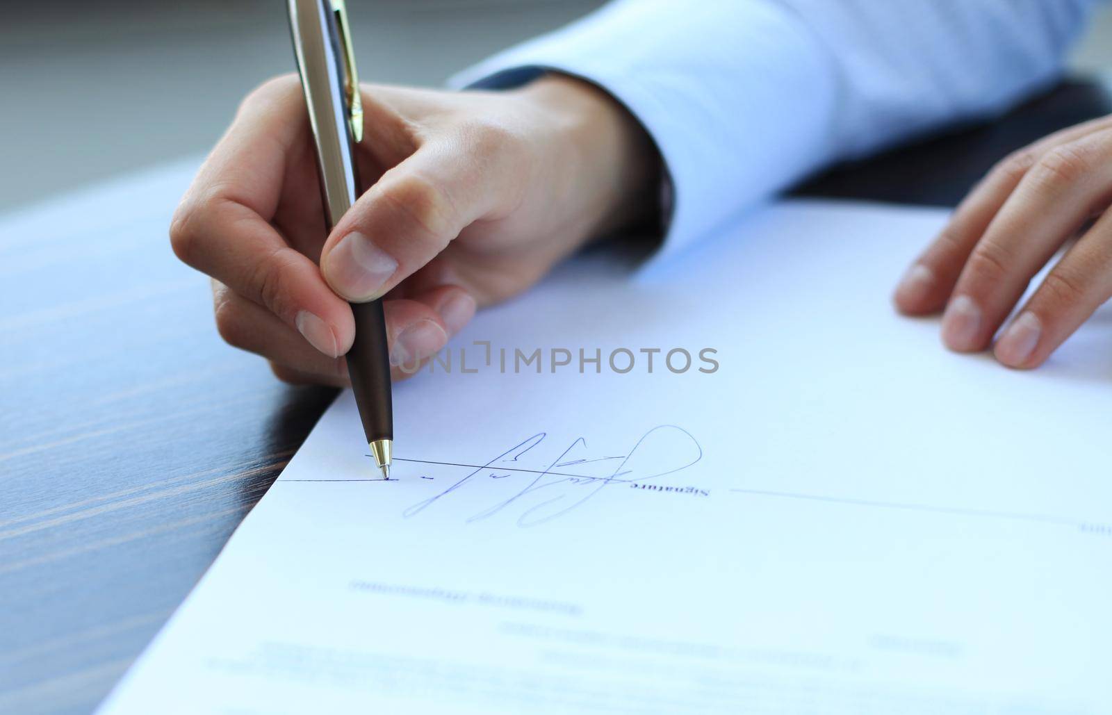 Businesswoman sitting at office desk signing a contract with shallow focus on signature.