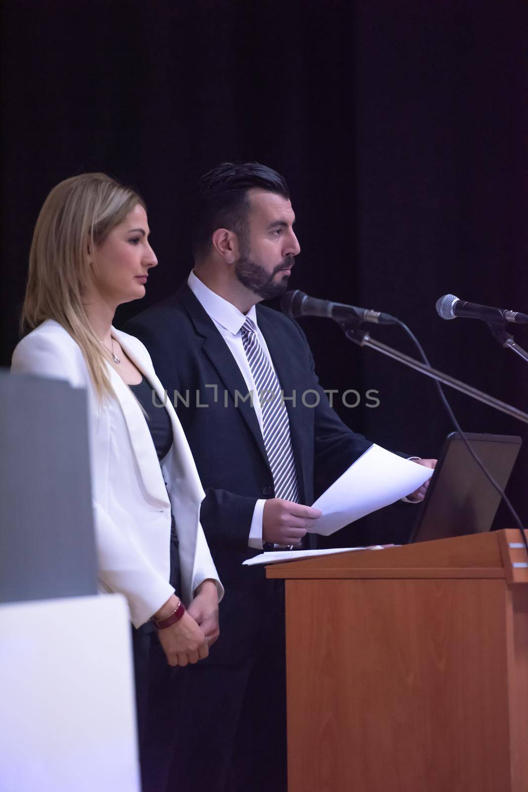 two young businesspeople giving a presentation to a group of colleagues seated in chairs at conference room