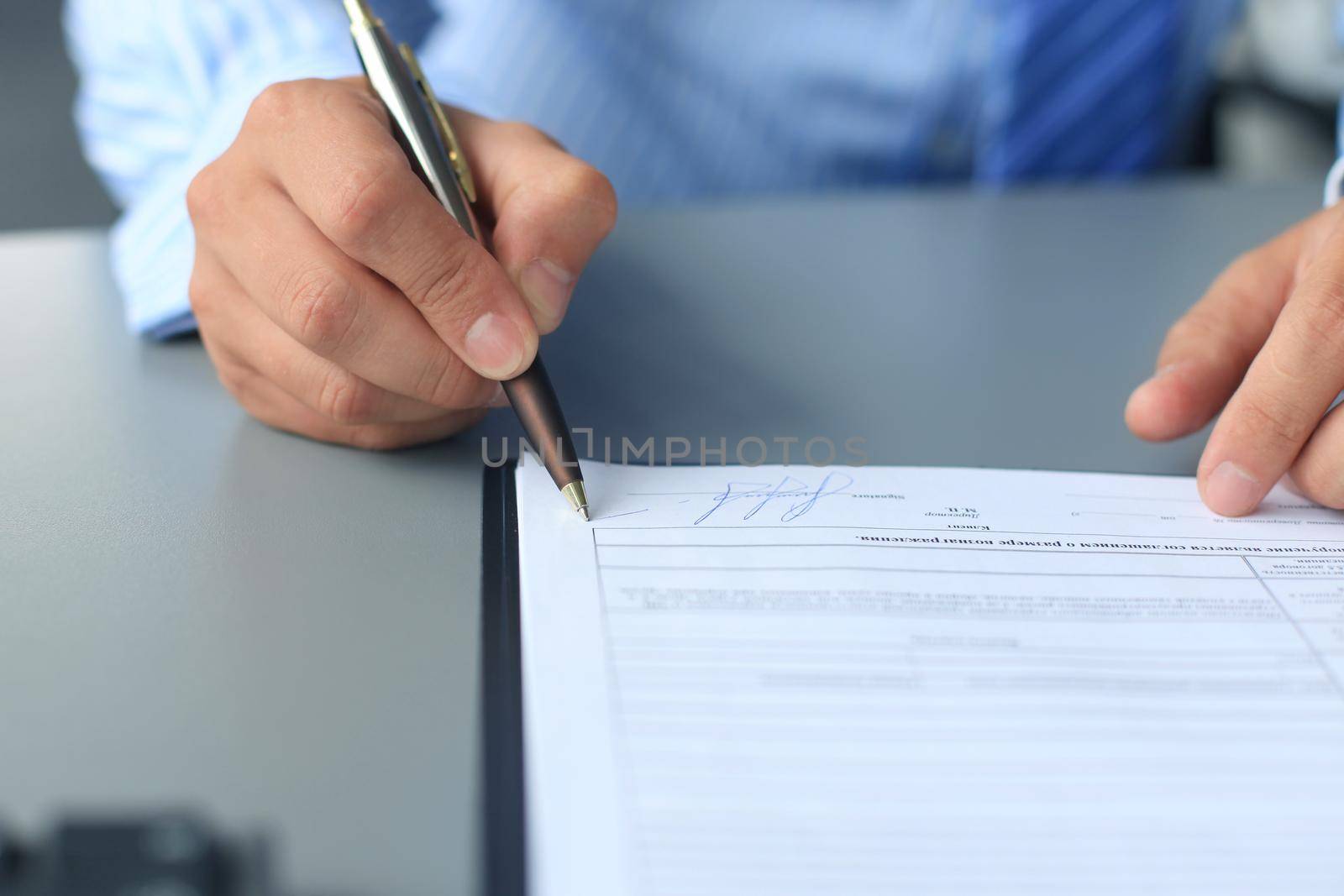 Businessman sitting at office desk signing a contract with shallow focus on signature. by tsyhun