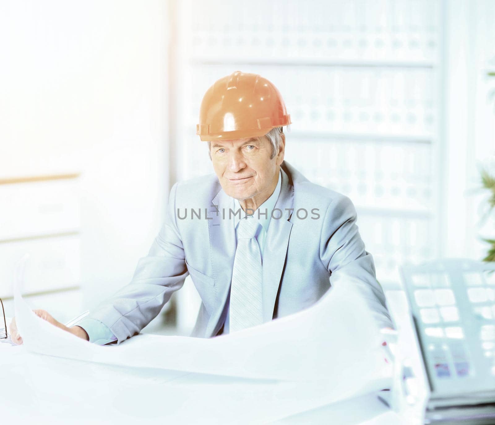 Portrait of professional architect with blueprints sitting behind table