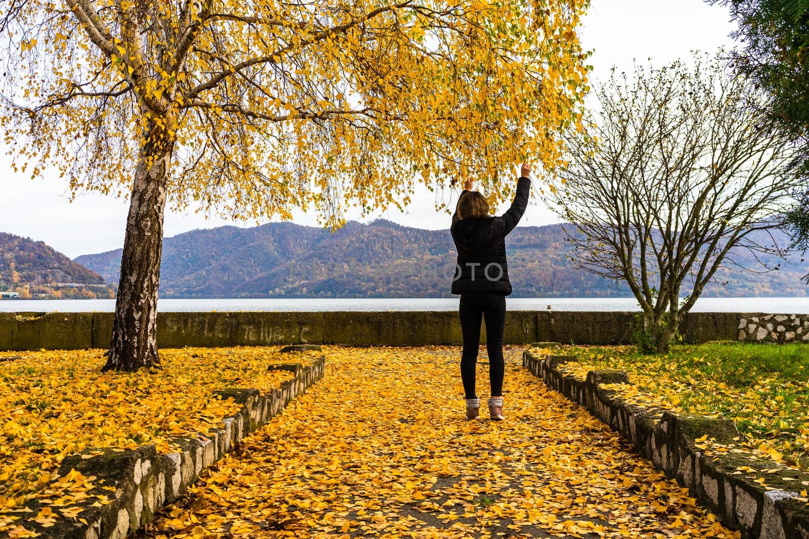 Autumn leaves fallen on alone woman walking on the autumn alley. Autumn landscape, orange foliage in a park in Orsova, Romania, 2020