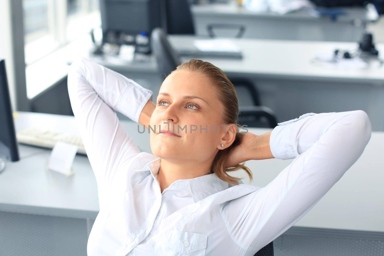 Business woman is relaxing with her hands behind her head and sitting on a chair in office by tsyhun