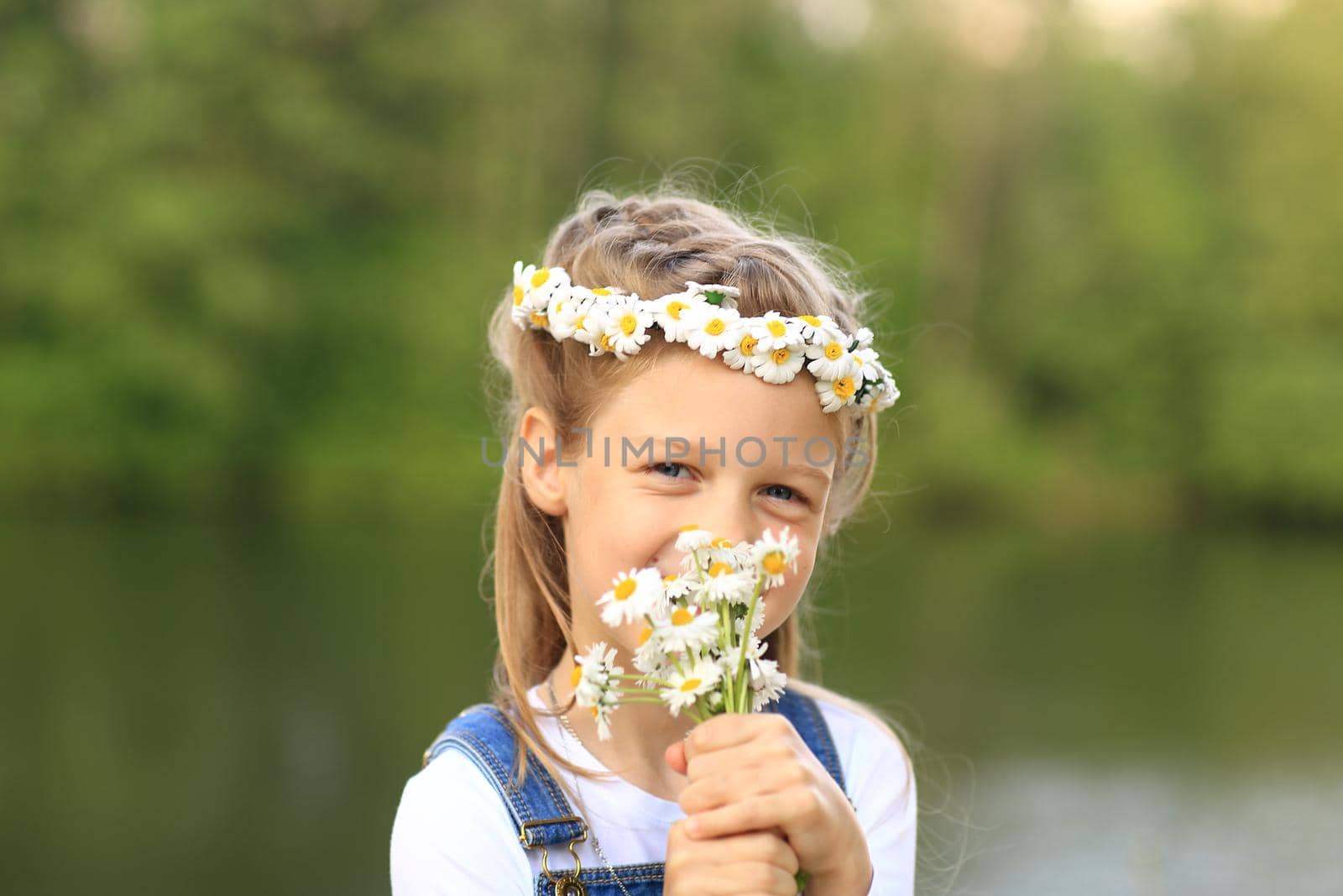 little girl in a wreath with a bouquet of flowers near the river in the Park on a Sunny day