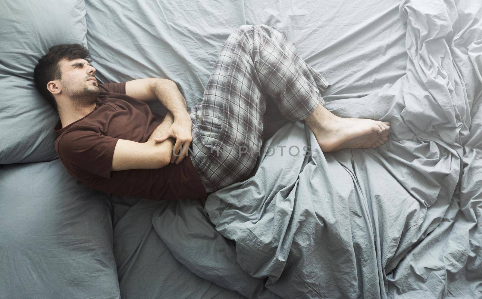 Man lying in bed having abdominal pain, top view by Prostock-studio