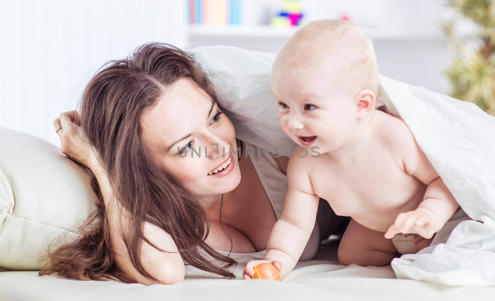 concept of happy mothers: happy mother and her year-old child playing on the sofa in the bedroom by SmartPhotoLab