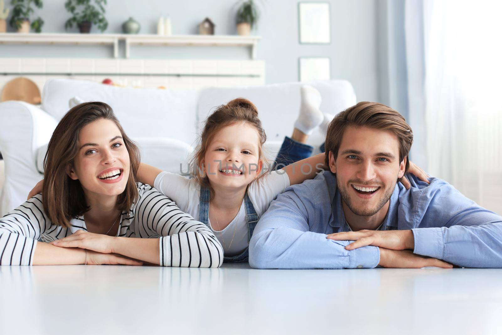 Young Caucasian family with small daughter pose relax on floor in living room, smiling little girl kid hug embrace parents, show love and gratitude, rest at home together