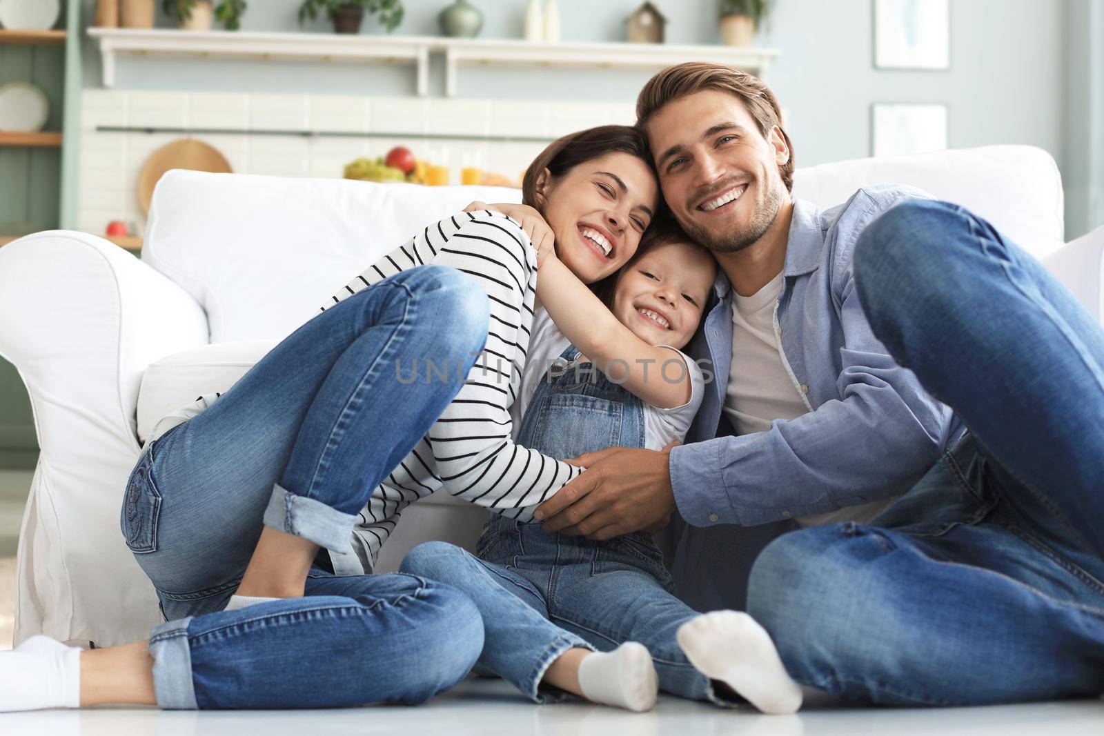Young Caucasian family with small daughter pose relax on floor in living room, smiling little girl kid hug embrace parents, show love and gratitude, rest at home together. by tsyhun