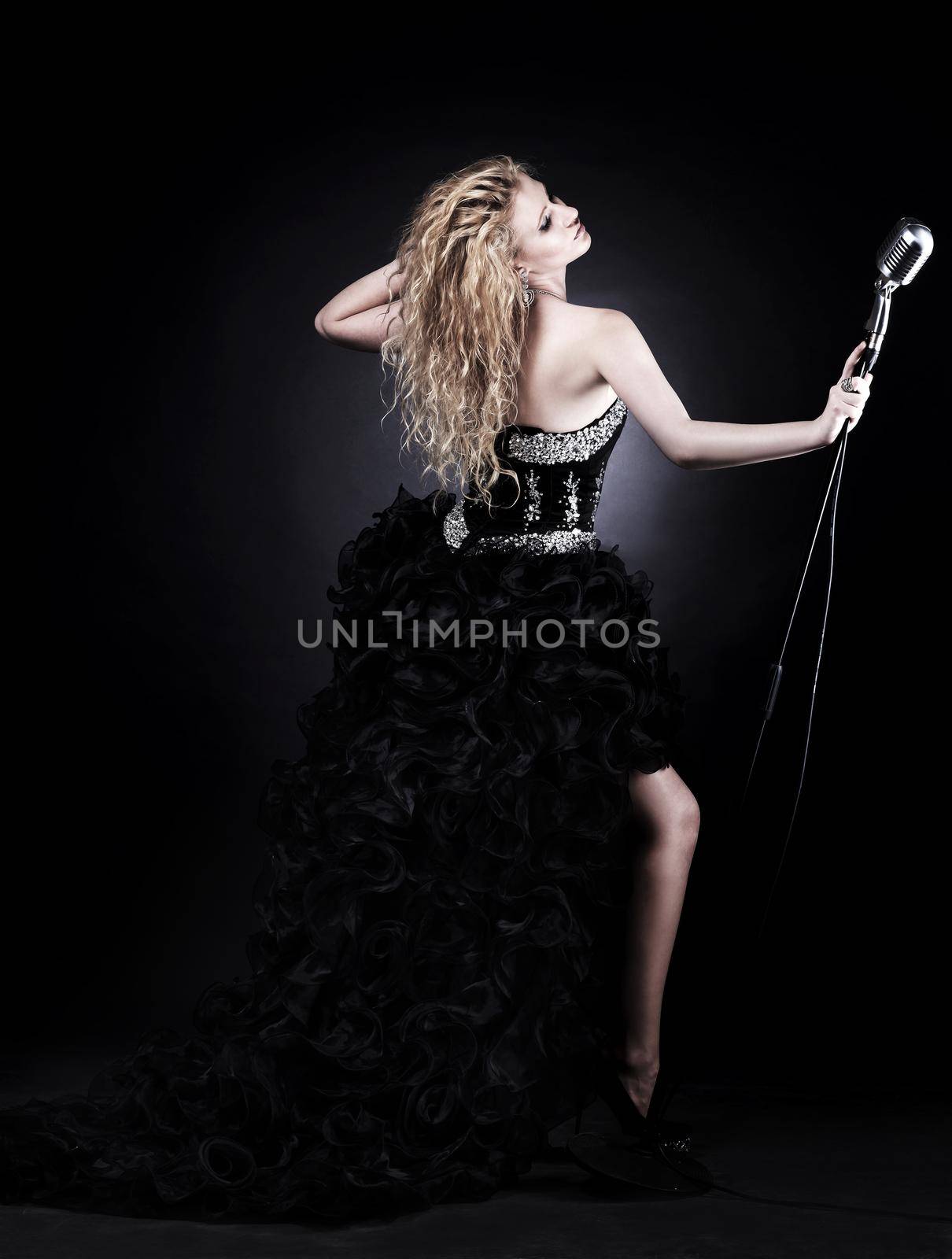portrait of a beautiful girl singer in black dress with in the microphone