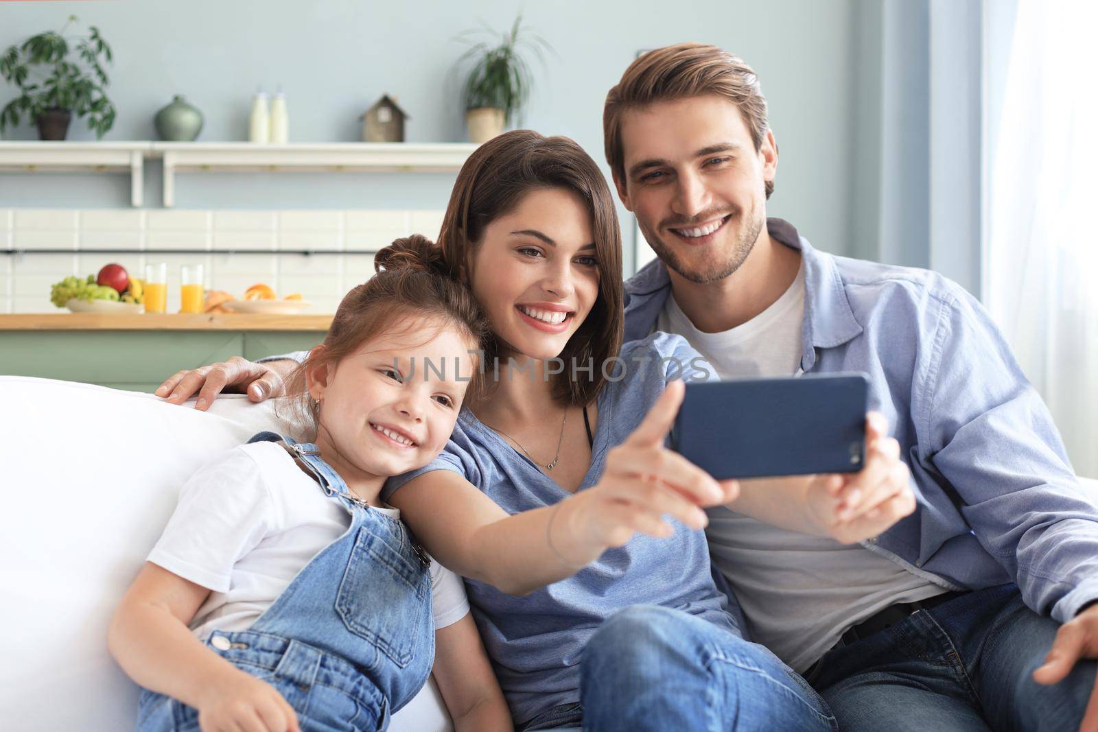 Beautiful young family with little child taking a selfie with a smartphone at home on the couch. by tsyhun