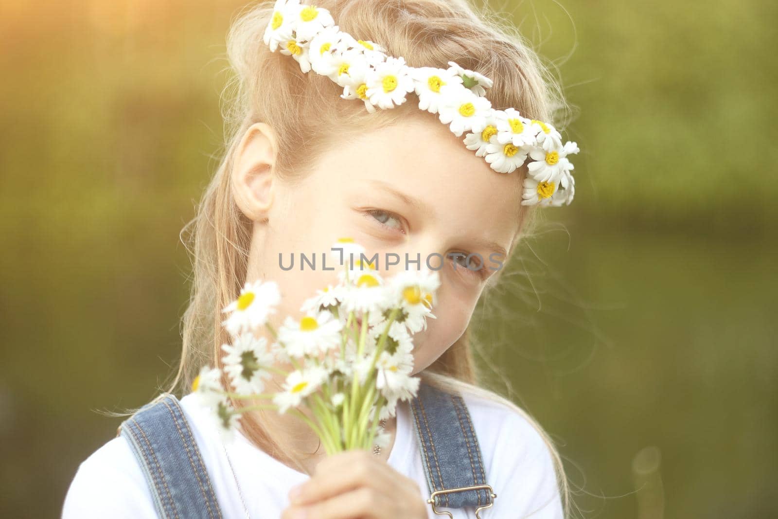little girl in a wreath of daisies and a bouquet of flowers in the Park on a Sunny day