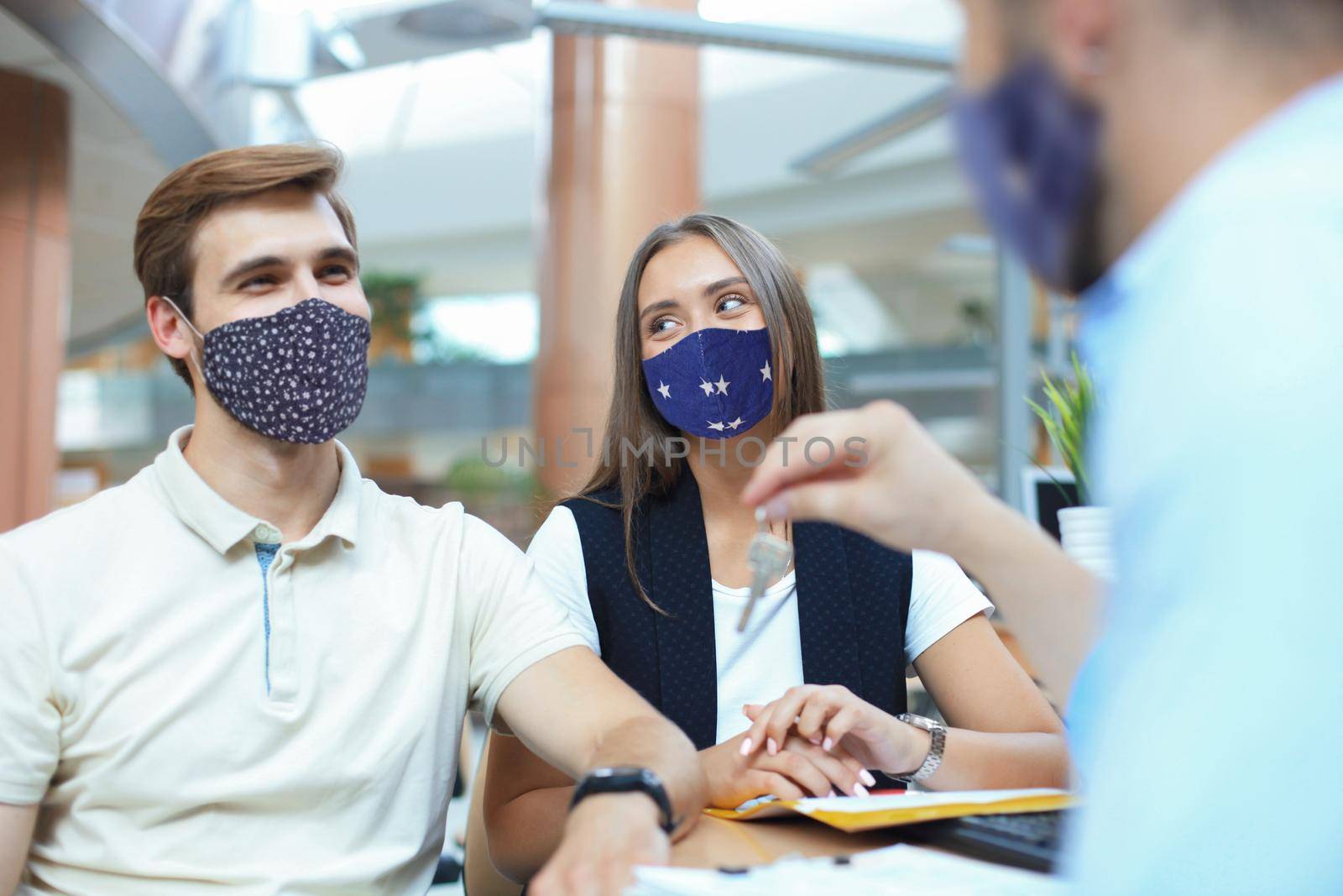 Close up of real estate agent giving keys to couple of customers in protective masks