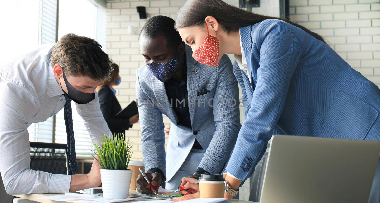 Business people wear preventive masks during epidemy in office. Collegues analysis finance growth success on meeting in office brainstorming, working on computers