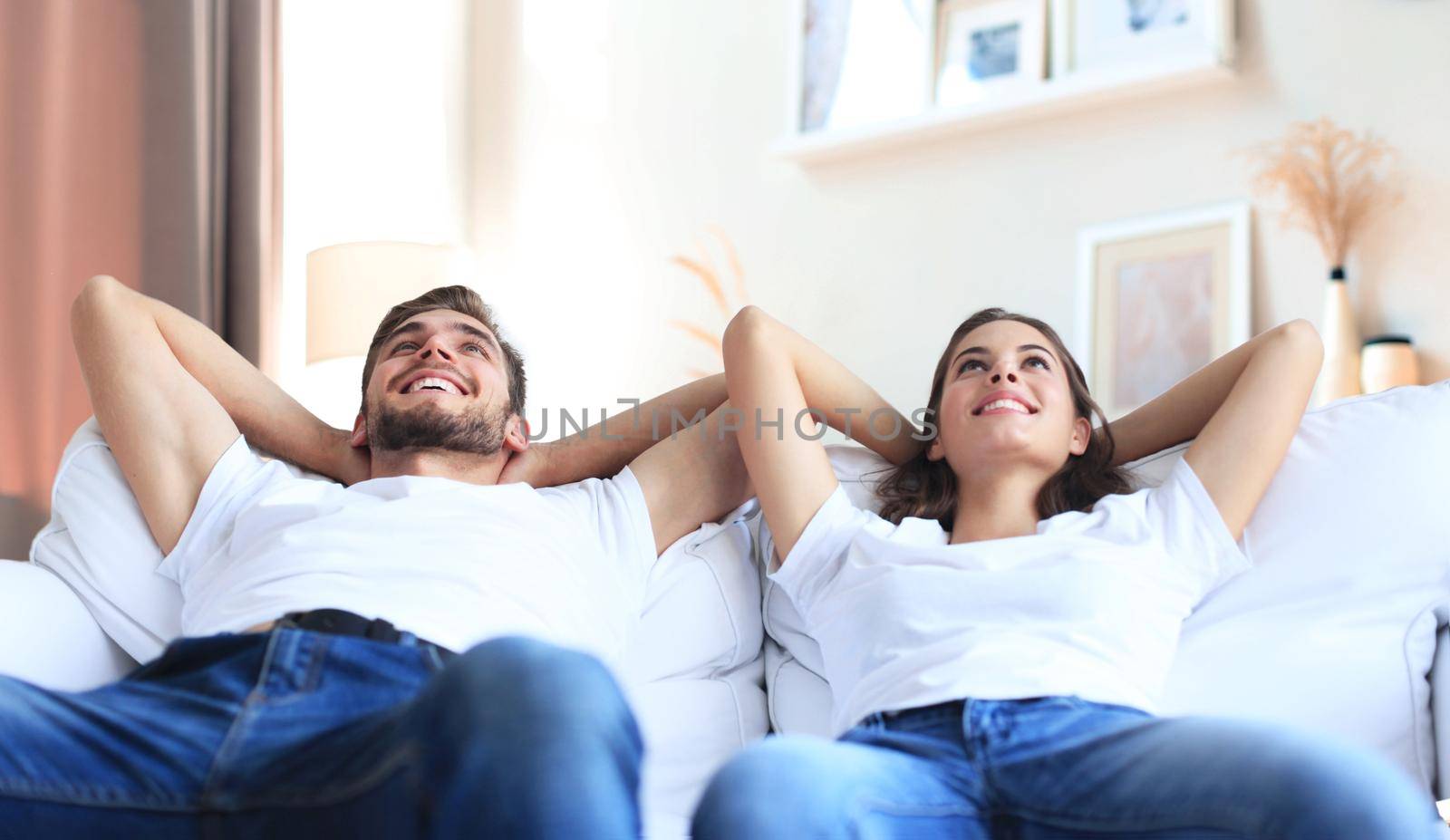 Smiling beautiful couple sitting on a sofa and dreaming about new home. by tsyhun