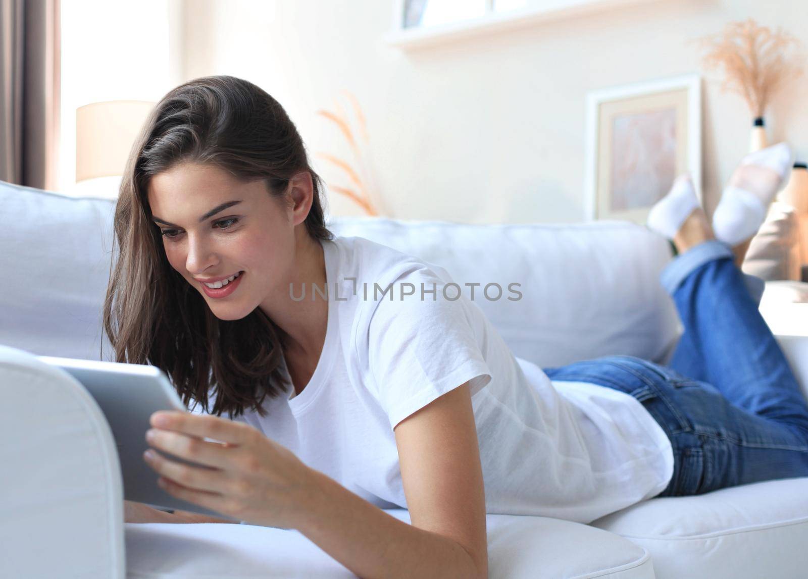 Beautiful young woman using tablet sitting on sofa at home at living room. by tsyhun