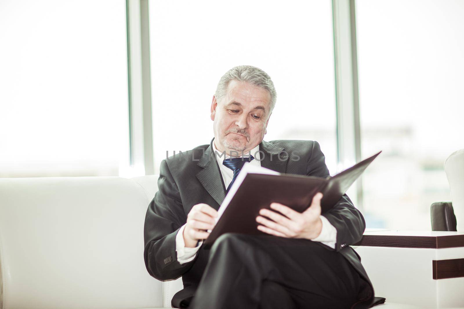 experienced lawyer reviews the documents with the terms of a new contract sitting on the sofa in the private office.