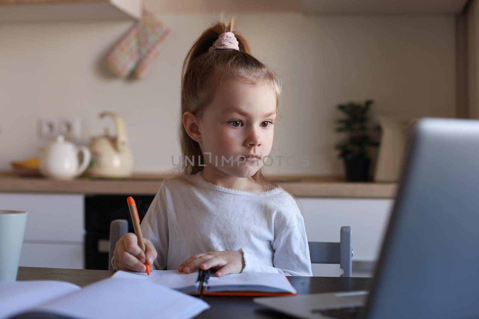 Serious little girl handwrite study online using laptop at home, cute happy small child take Internet web lesson or class on PC