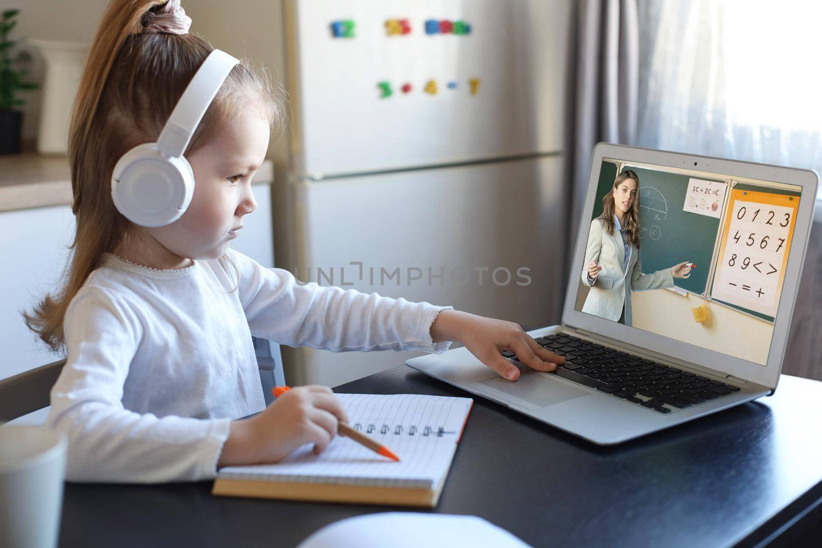 Smart small preschooler girl in headphones watch online lesson and communicate with teacher at home, little child in earphones study on Internet using laptop wireless connection
