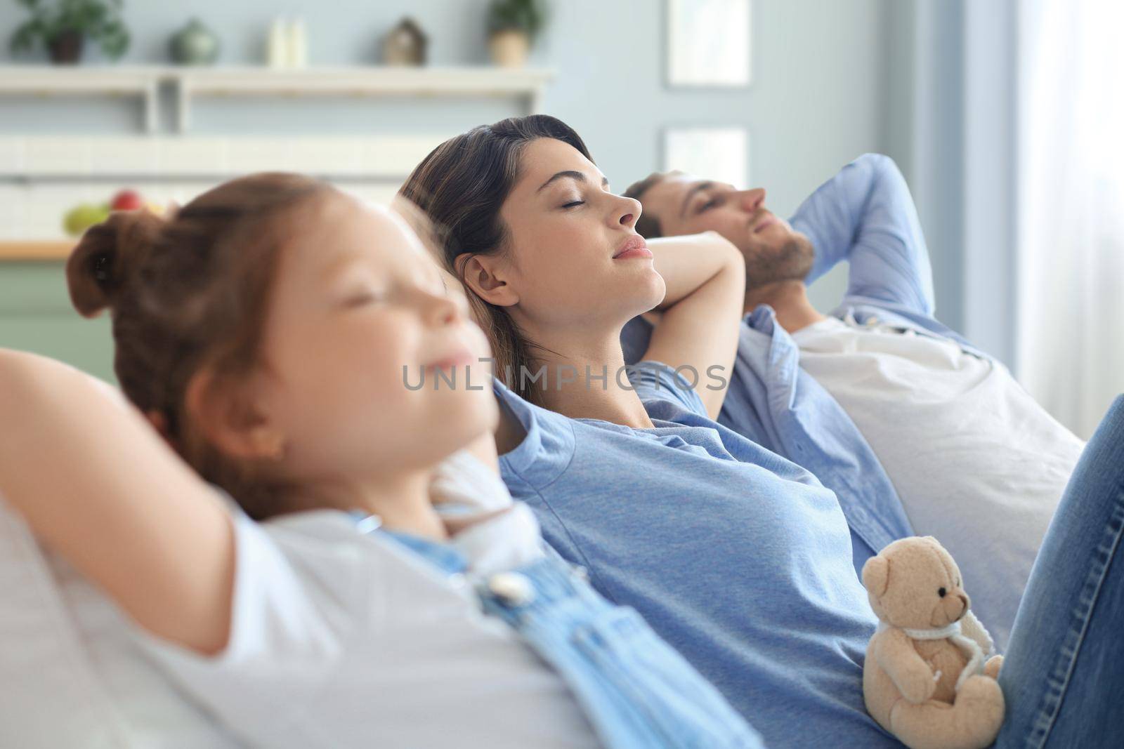 Relaxed young family resting and dreaming about new home on comfortable sofa together at home, happy young parents with little daughter relax enjoying nap relaxing or meditating. by tsyhun