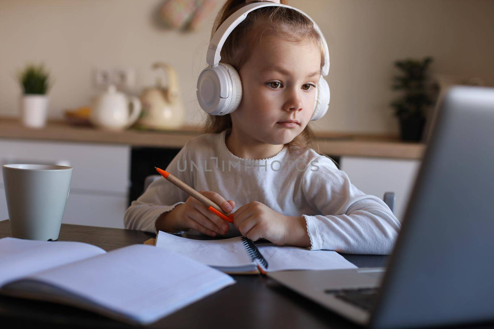 Smiling little girl in headphones handwrite study online using laptop at home, cute happy small child in earphones take Internet web lesson or class on PC. by tsyhun