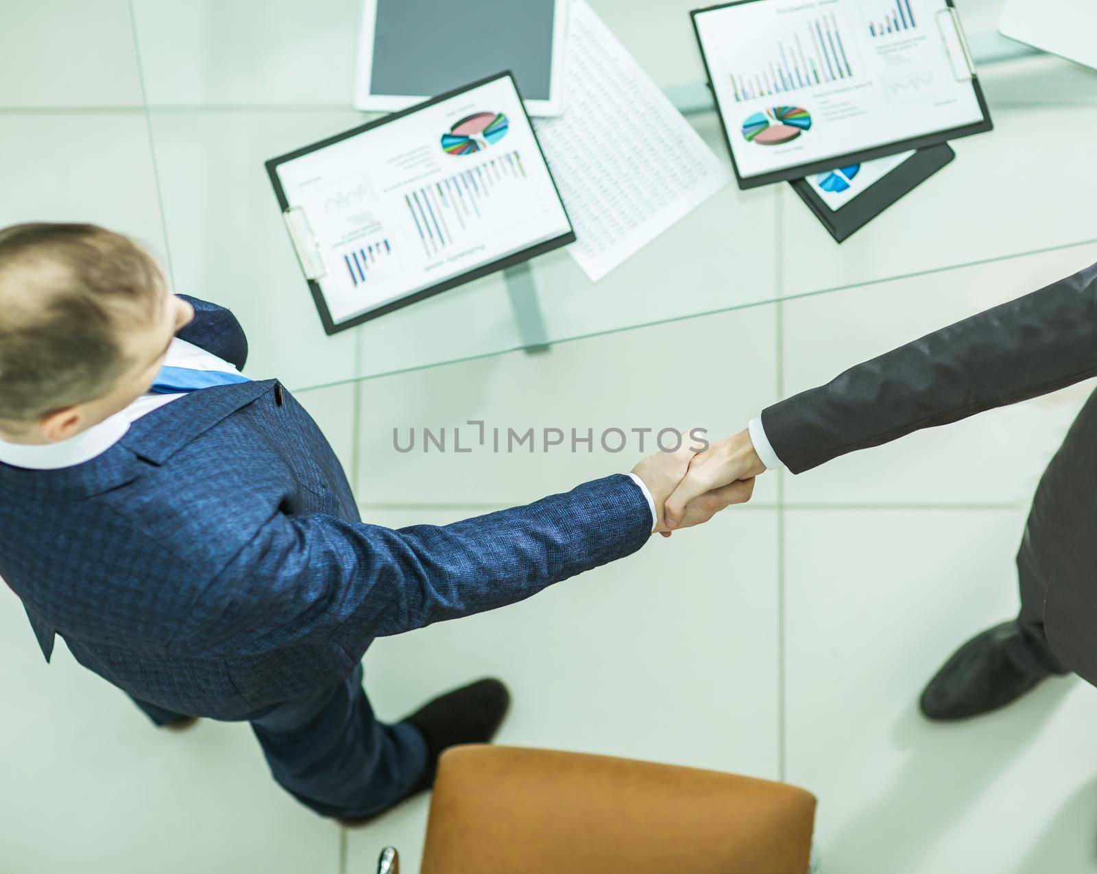 handshake business partners near the desktop, with the financial schedules.