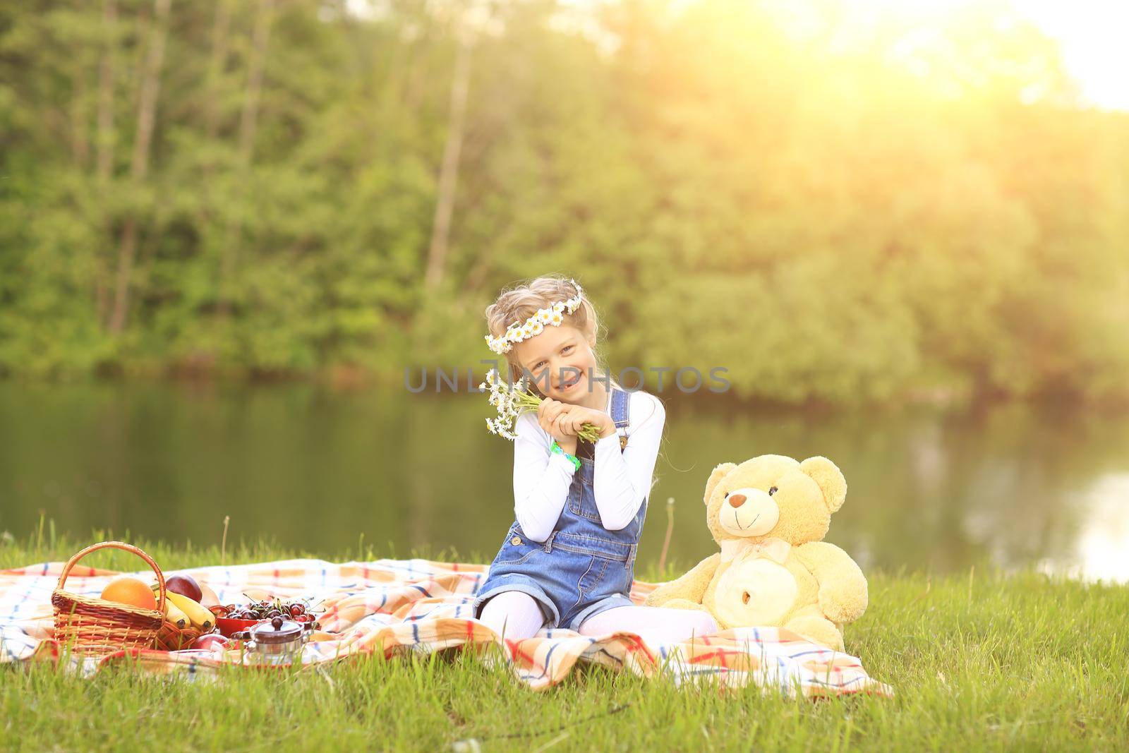 little girl with a soft toy on a picnic near the river on a Sunny day