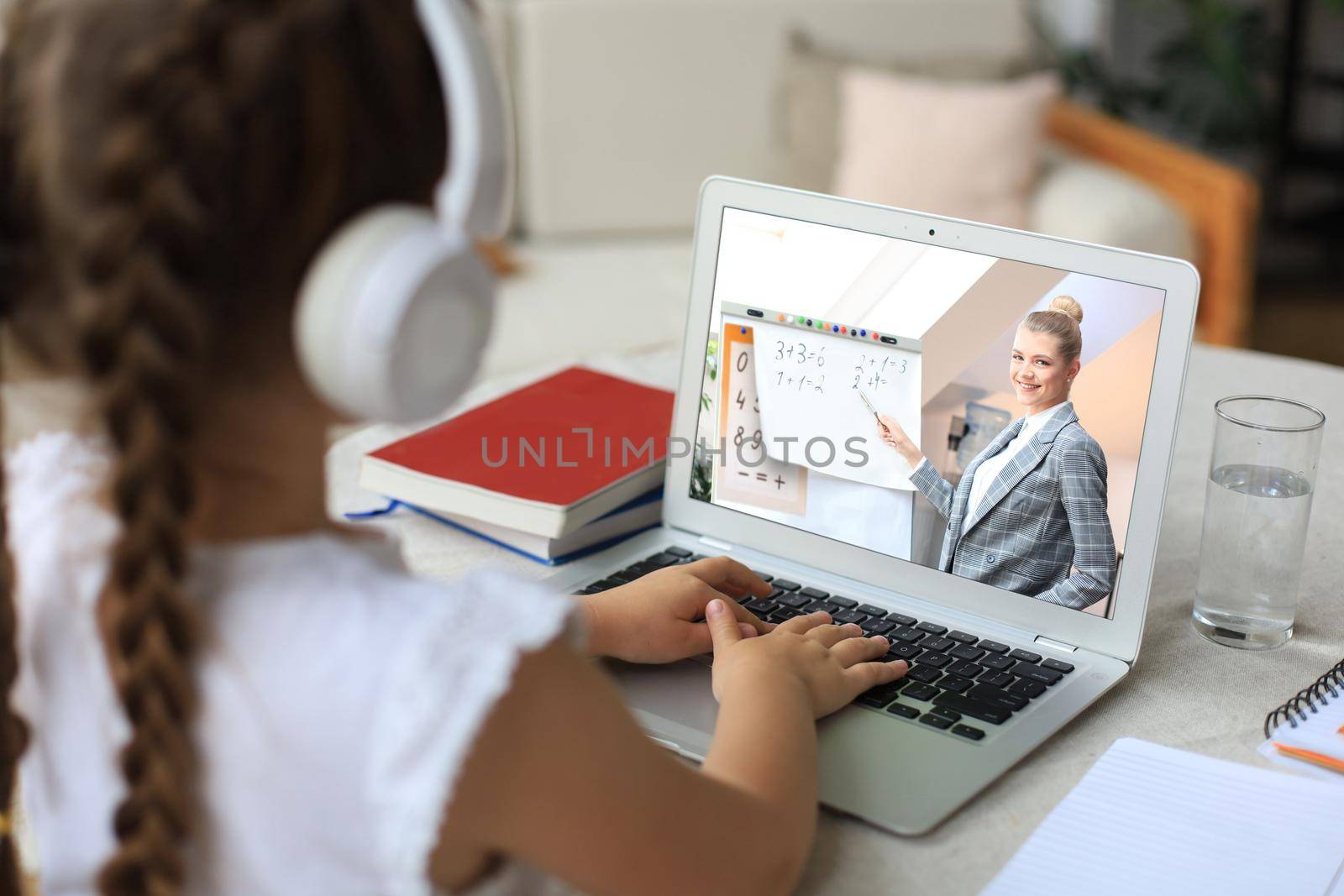 Distance learning. Cheerful little girl girl in headphones using laptop studying through online e-learning system