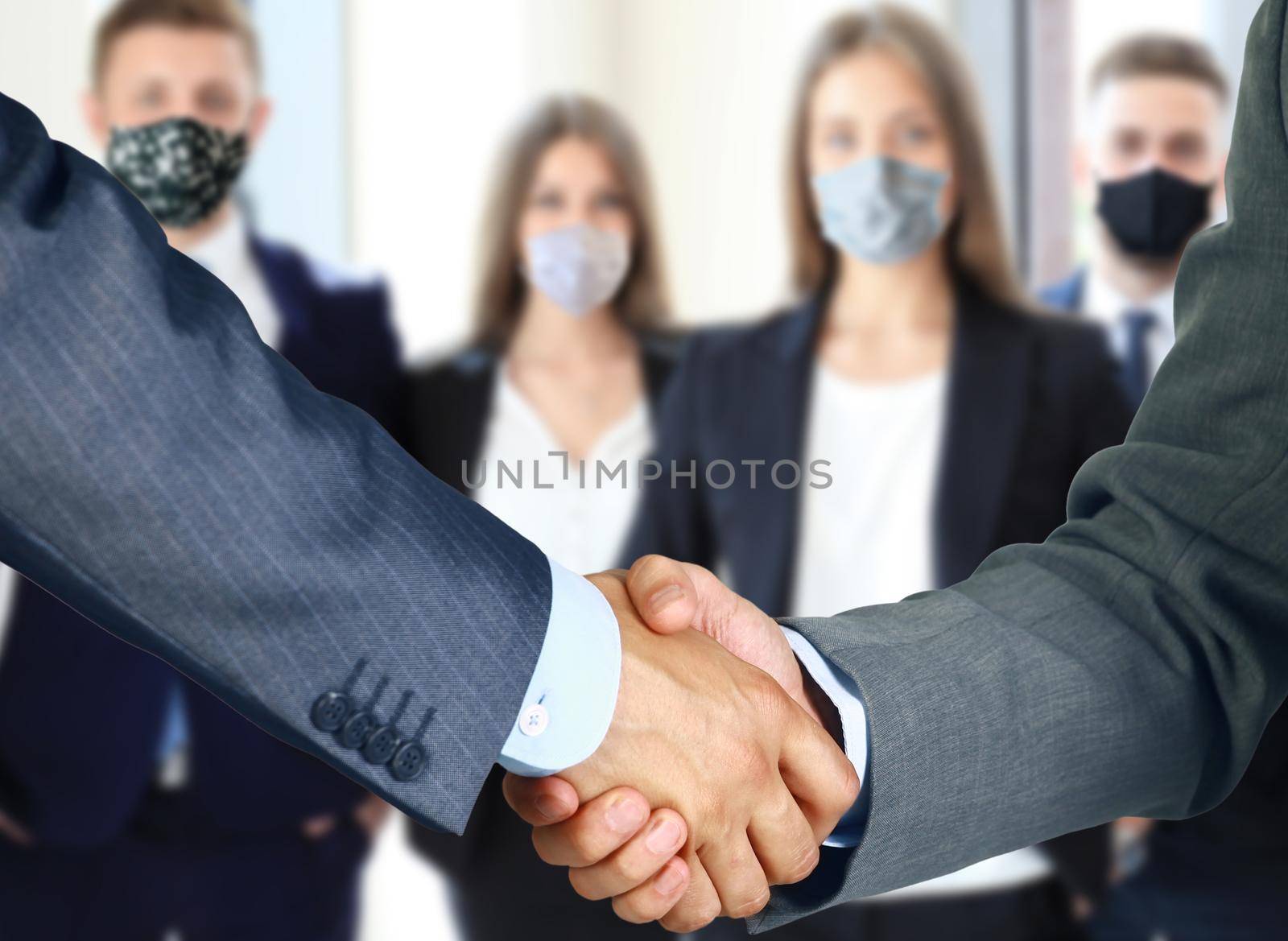 Business people in protective masks shaking hands, finishing up a meeting. by tsyhun