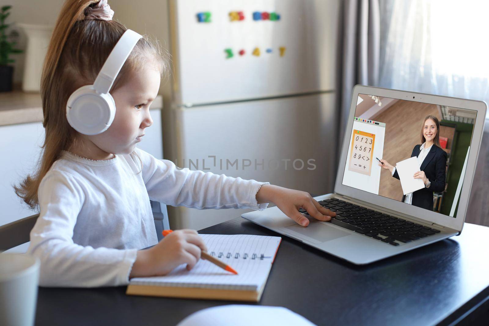 Distance learning. Cheerful little girl girl in headphones using laptop studying through online e-learning system. by tsyhun