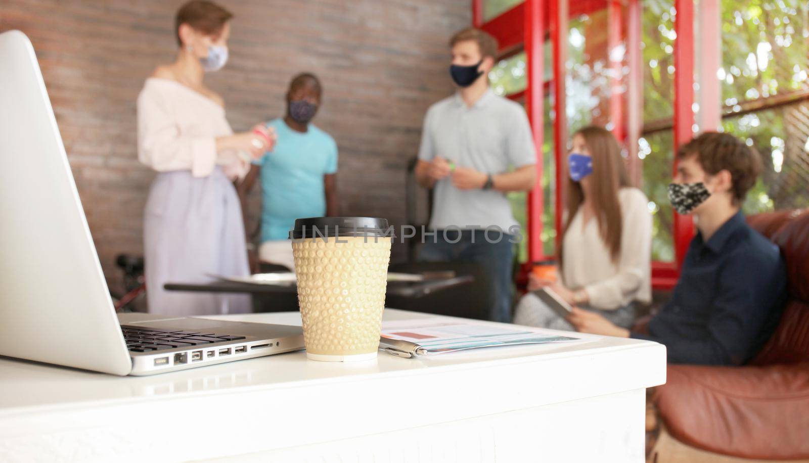 Group of young business people in preventive masks discussing something while working in the creative office